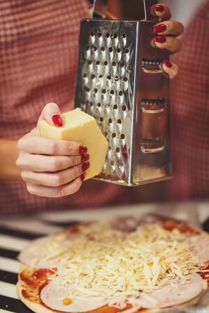 Close-up of a young women's hands grating cheese and putting it on the pizza.の写真素材