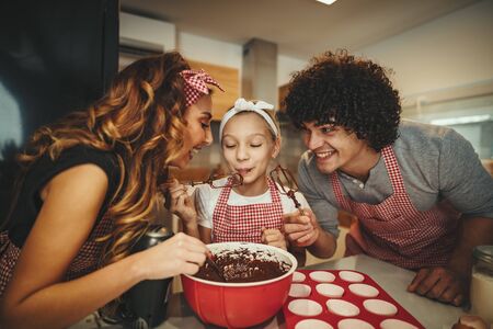 Happy father and his daughter are preparing cookies together in the kitchen. Father is pouring...