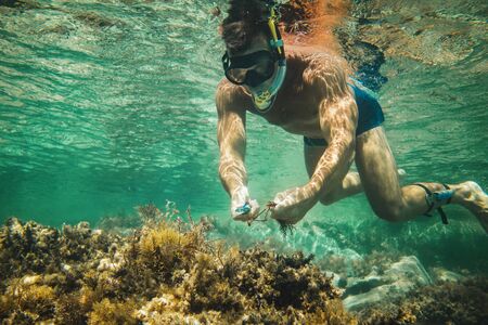 Handsome man having fun at summer vacation and exploring seafloor during scuba diving in sea.の写真素材