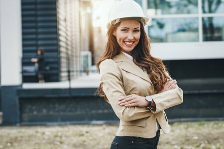Young successful female engineer with white helmet is standing against urban city background.の写真素材