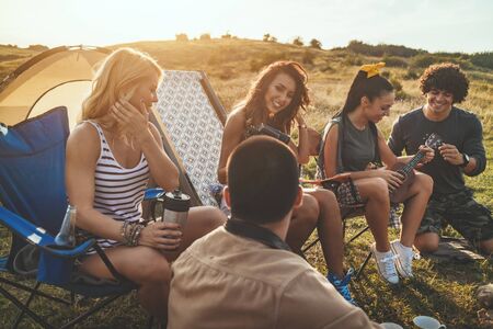 Young people have a good time in camp in nature. They're resting, laughing and singing with music...