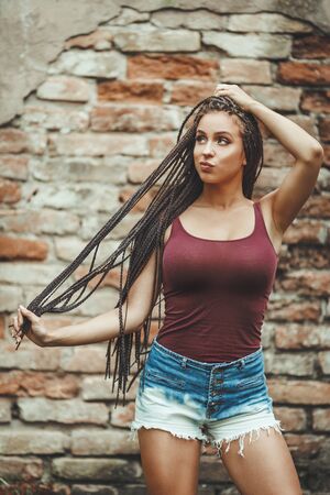Pretty young caucasian woman with long afro braided hair is standing against the brick wall and pouting her lips.の写真素材