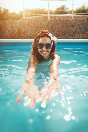 Beautiful smiling happy young woman is enjoying in swimming pool. She is ready to swim in clear blue...