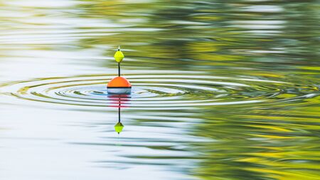 A fishing float floats on the water of the lake making circles in the waterの写真素材