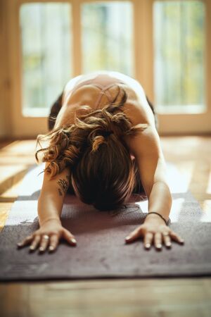 Young woman is doing yoga meditation during coronavirus pandemic in the living room at home. She is...