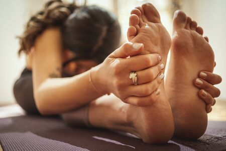 Close up of a young woman is doing stretching exercise on floor mat in morning sunshine. She is...