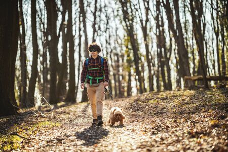 Happy smiling handsome man is walking along the forest path with his dear cute dog enjoying landscape in forest in beautiful sunny day.の写真素材