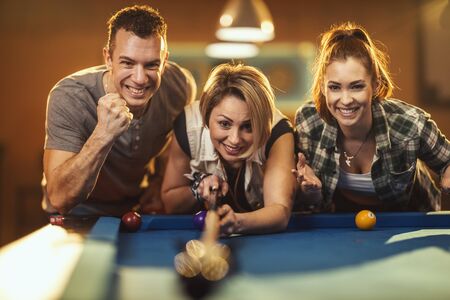 Group of a four smiling cheerful friends are playing billiards in bar after work. They are involved in recreational activity.の写真素材