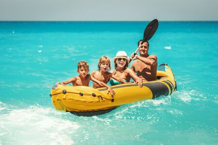 Happy family is enjoying a ride in rubber kayak and waves are splashing them at tropical ocean water during summer vacation.の写真素材