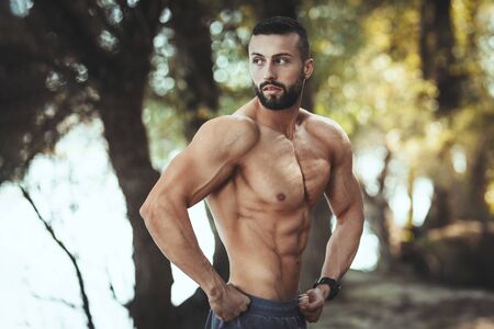 Fit muscular young man with naked torso is posing in the nature near the river.の写真素材