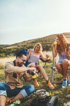 Happy young friends enjoy a sunny day in nature. They're cooking tea, laughing and talking happy to be together.の写真素材