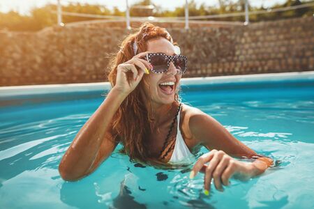 Beautiful cheerful  young woman is enjoying in swimming pool. She is ready to swim in clear blue water.の写真素材