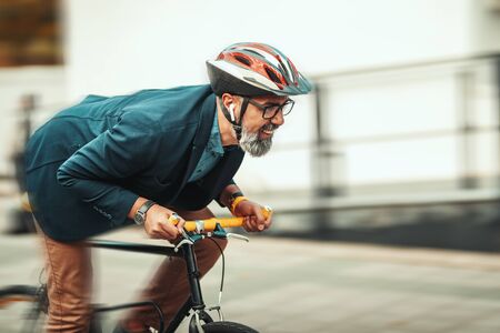 A handsome casual middle-aged businessman is going to the office by bicycle. He is hurrying up because he is late.の写真素材