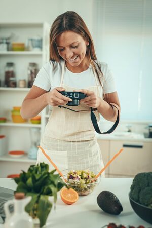Beautiful young woman taking photo of healthy salad with digital photo camera for her vlog.の写真素材
