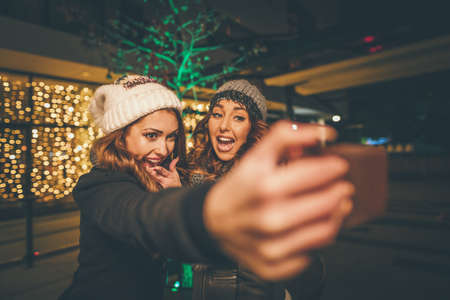 Cheerful young female friends are having fun and taking funny selfie in city street at  the night.の写真素材