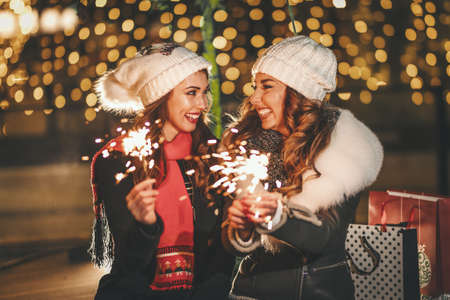 Cheerful young sisters are holding sparklers and having fun at holiday winter night in the city street.の写真素材