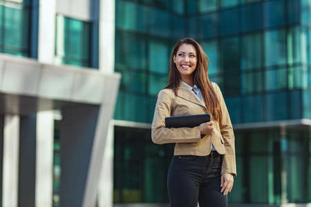 Beautiful young successful smiling woman is walking on the way through the office district against urban city background.の写真素材