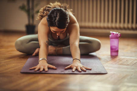 Young woman is doing yoga meditation during coronavirus pandemic in the living room at home. She is...