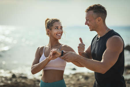 A beautiful young woman and handsome man are ready to do jogging along the sea path in sunrise.