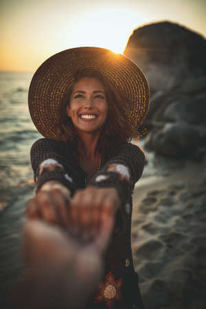 A beautiful young woman is having fun and relaxing on the beach at the sunset. She extends hands to...