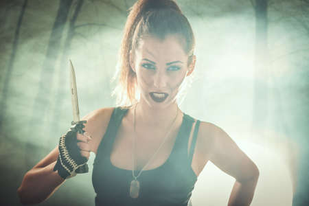 Beautiful soldier woman is holding combat knife and getting ready for the attack and looking at the...