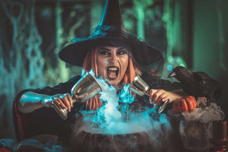 A witch in foggy surrounding holds two goblets above boiling water for a cooking poison soup.の写真素材