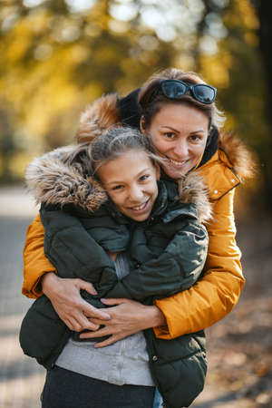 Beautiful mother and her happy teenage daughter are posing and having fun in the park, hugging and smiling.の写真素材