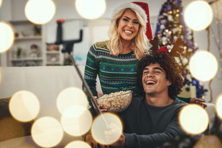 Loving couple dressed in cozy warm sweaters is spending time in the living room on Christmas - New...