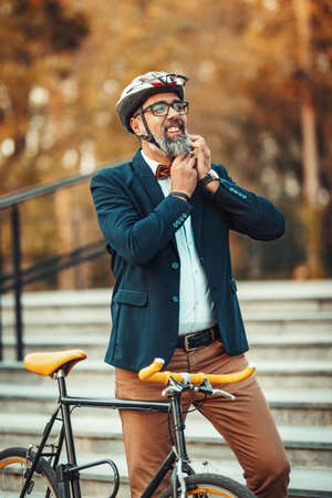 A handsome casual middle-aged man is going to go the ride by bicycle and he is putting his helmet on...