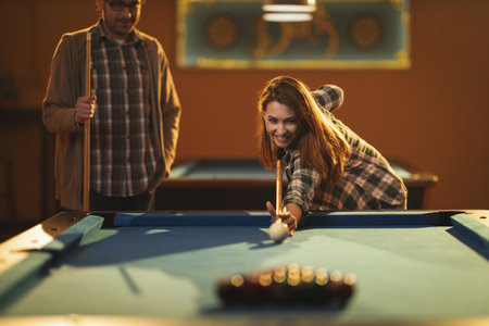 Young smiling cheerful woman are playing billiards in bar after work. She is involved in...