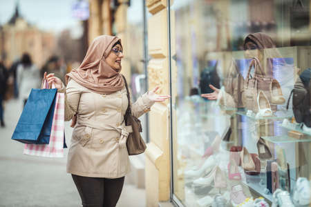 Middle aged Muslim woman wearing hijab with a happy face is walking in urban environment, going to the shopping holding paper colored bags.の写真素材