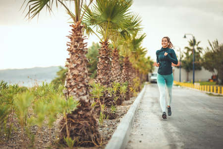 A beautiful woman is running along the path of a Mediterranean town by the sea and enjoying in summer sunny day.の写真素材