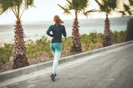 Rear view of a beautiful woman is running along the path of a Mediterranean town by the sea and enjoying in summer sunny day.の写真素材