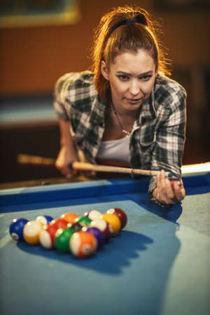 Concentrated young woman while playing billiards in billiard club after work.の写真素材