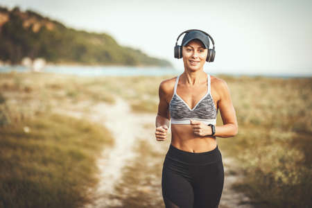 A beautiful smiling happy woman is running along the path near the sea and enjoying in summer sunny...