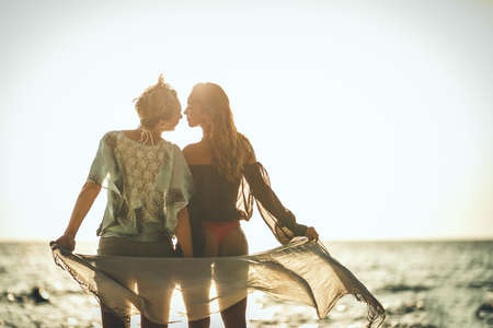 Beautiful two young women are having fun and relaxing on the beach at the sunset. They are posing...