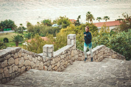A beautiful woman is running along the path of a Mediterranean town by the sea and enjoying in...