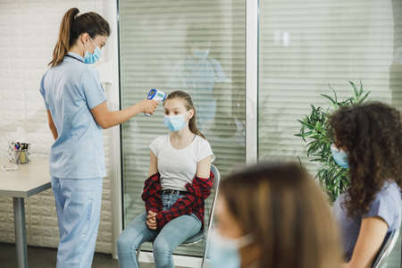 Female teenager with a face mask having her temperature checked before vaccine.の写真素材