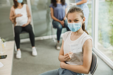 A cute teenager girl with a smile showing vaccination certificate after receiving the vaccine.の写真素材