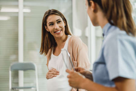 Attractive pregnant woman talking to nurse while waits for gynecologist check up.の写真素材
