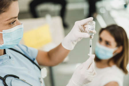 Nurse holding syringe and making  vaccination injection dose in shoulder of female patient wearing...