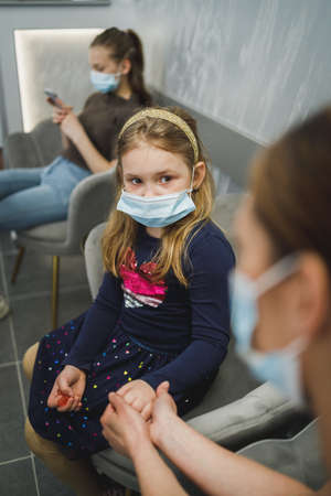Scared little girl and her mom with face mask in waiting room at dentist's office.の写真素材