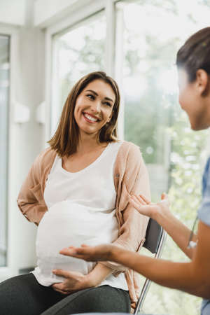 Attractive pregnant woman talking to nurse while waits for gynecologist check up.の写真素材