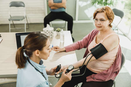 Nurse talking to senior woman and checking the blood pressure to her.の写真素材