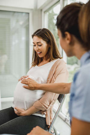 Attractive pregnant woman talking to nurse while waits for gynecologist check up.の写真素材