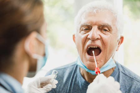 A senior man having swab medical test from throat during coronavirus pandemic.の写真素材