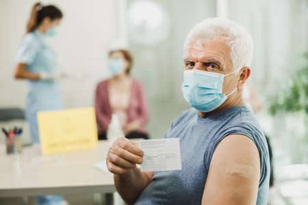 A senior man showing vaccination certificate after receiving the Covid-19 vaccine. Looking at camera.の写真素材