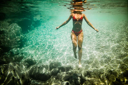 A beautiful young woman is swimming underwater enjoying the blue of the sea.の写真素材