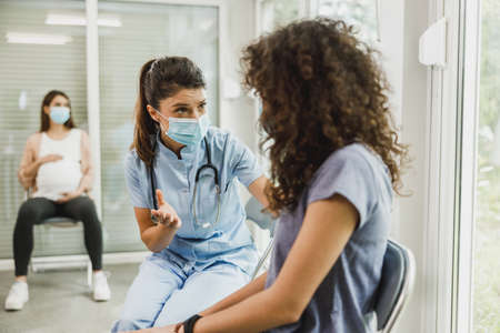 Nurse talking to African American teenager girl in a waiting room while she waits for gynecologist...