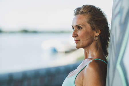 Portrait of a middle age sportswoman resting after training near the river and pensive looking into the distance.の写真素材